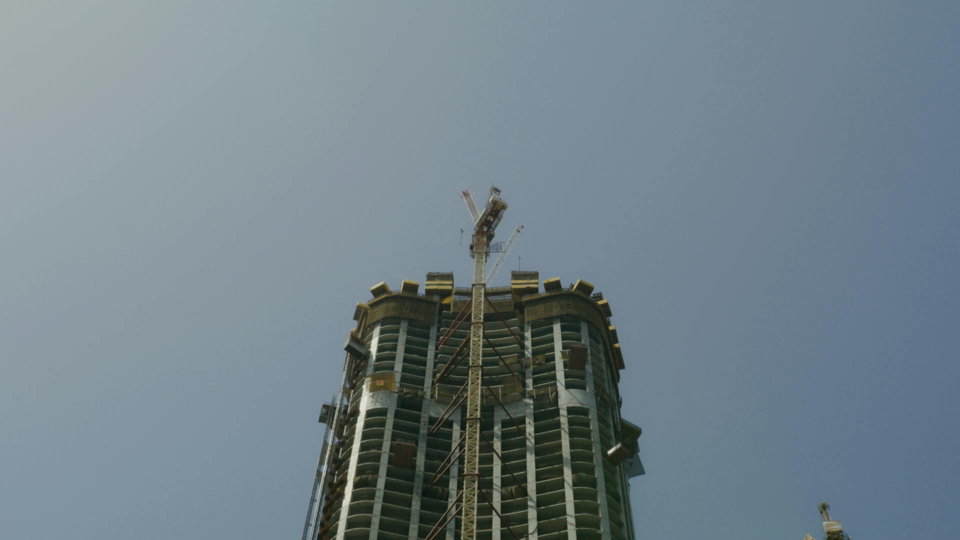 A tall skyscraper under construction with a crane against a blue sky in Dubai.