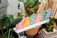 Round shaped letters with Easter title between green plants and decorative bunny on pile of books at home