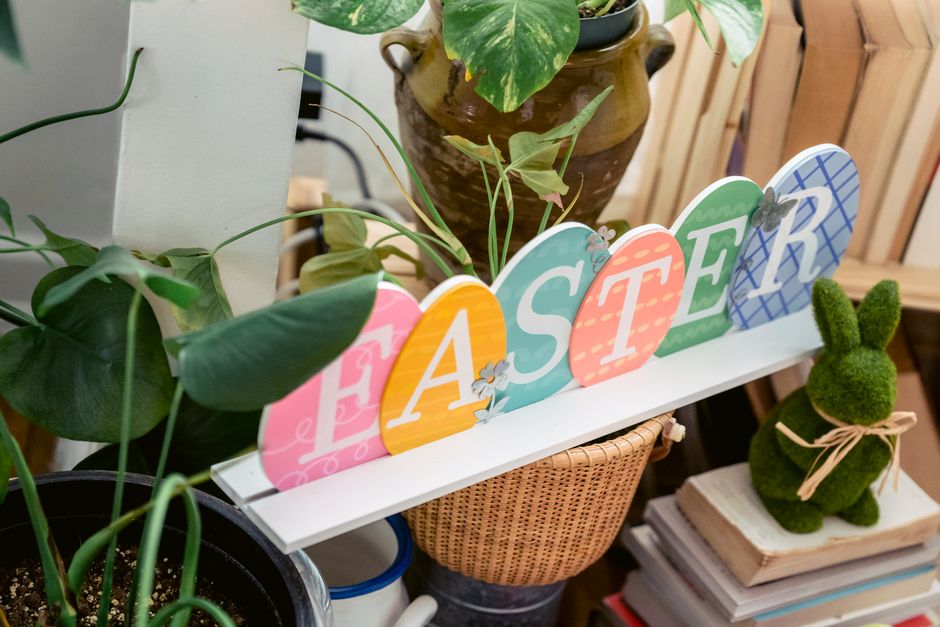 Round shaped letters with Easter title between green plants and decorative bunny on pile of books at home