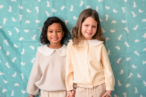 Cheerful multiethnic kids in similar outfit holding hands while looking at camera against cloth with hare ornament