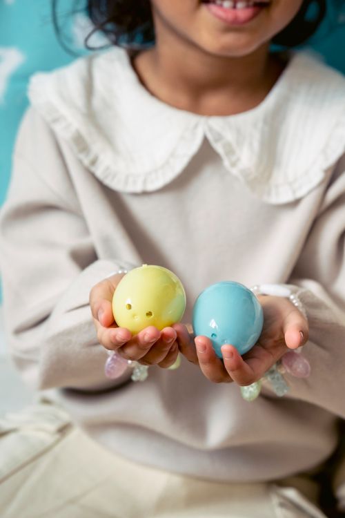 Free Crop cheerful ethnic kid in wear with collar showing colorful painted eggs during festive event Stock Photo