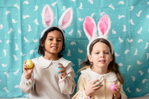 Charming multiracial kids in hairbands with decorative hare ears and painted eggs looking at camera on Easter Day