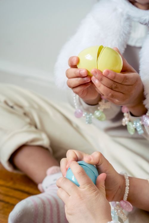 Free Crop unrecognizable girls in casual wear playing with colorful surprise toy eggs and sitting on floor Stock Photo