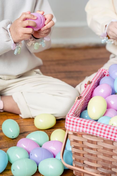 Free Crop unrecognizable little girls playing with colorful surprise toy eggs while sitting on floor near wicker basket Stock Photo