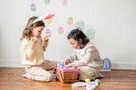 Side view of adorable little Hispanic girl choosing colorful Easter eggs while playing with friend on floor at home