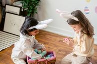 Adorable small girls enjoying game with plastic eggs in wicker basket on timber floor in daylight