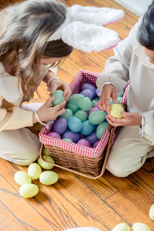 Free From above of crop anonymous multiracial girls placing plastic eggs into wicker basket on timber floor Stock Photo
