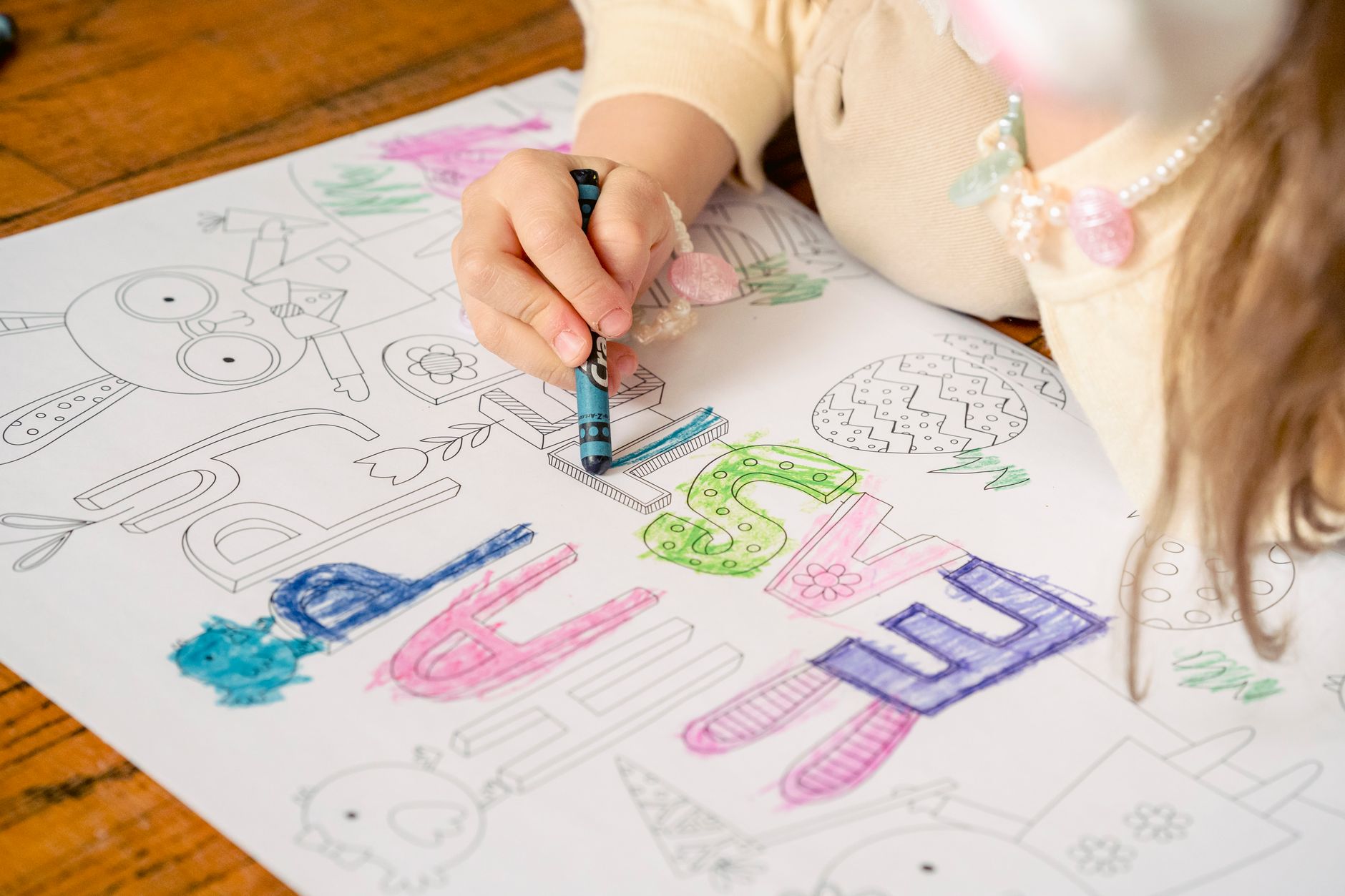 Girl coloring letters on greeting saying happy Easter