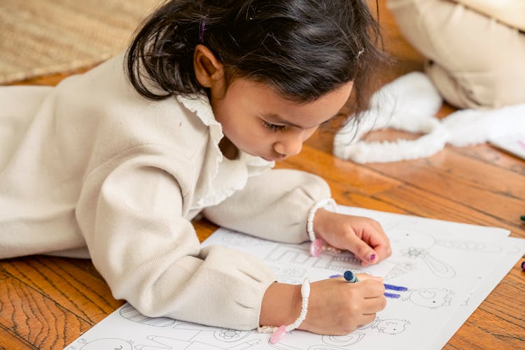 Calm Ethnic Girl Lying On Floor And Drawing In Coloring Book