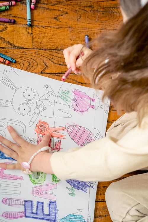 Free High angle of crop anonymous little girl sitting on floor and paining in coloring book in room in daylight Stock Photo