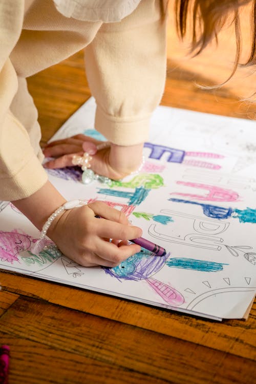 Crop anonymous girl in casual clothes drawing in coloring book at home in daytime