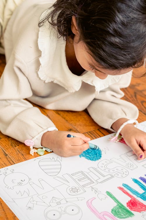 Concentrated little girl painting in coloring book at home