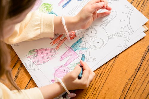 Free From above of crop unrecognizable girl in casual clothes drawing in coloring book in daylight Stock Photo