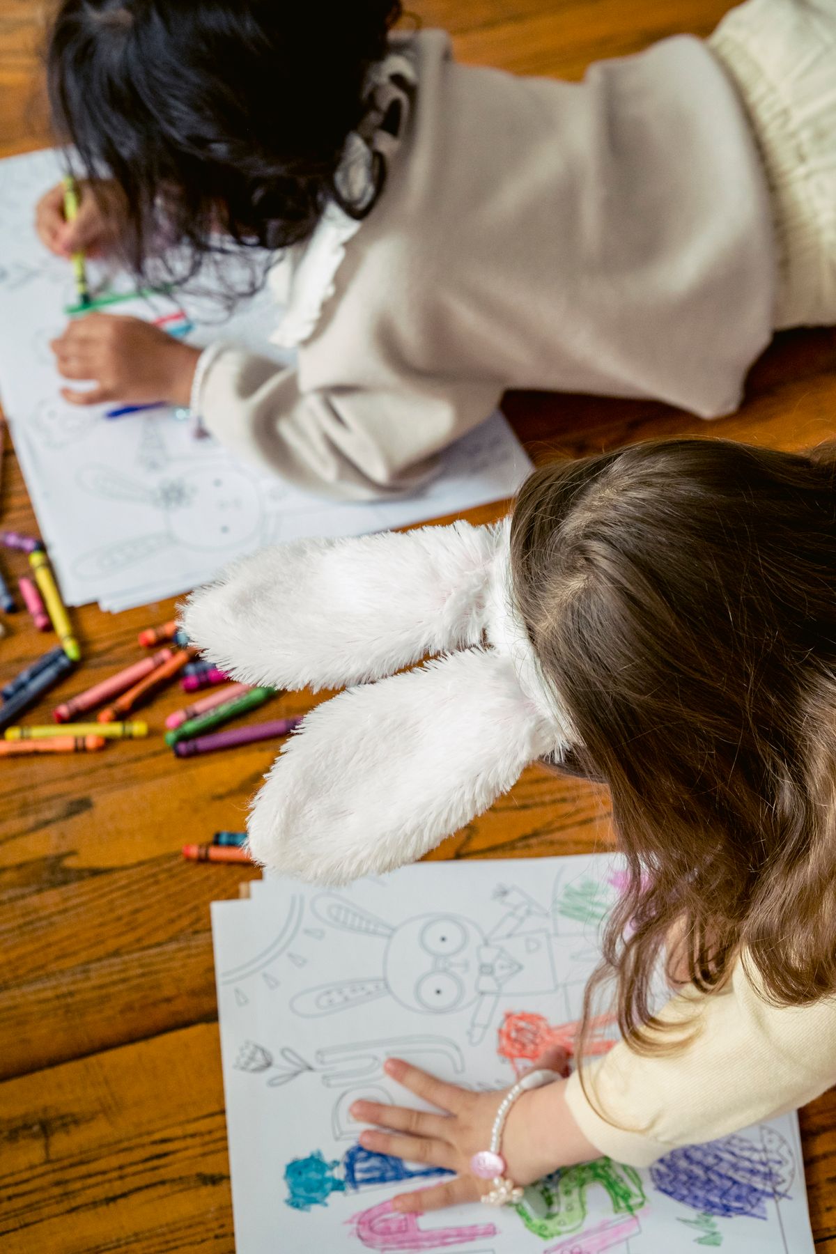 Kids coloring bunny pictures with wax crayons on paper at a table