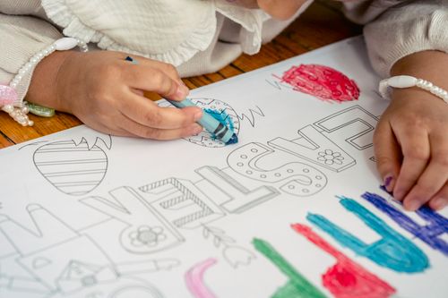 Free High angle of crop unrecognizable child on wooden floor drawing Happy Easter words and eggs with wax pencil in arm in bright room Stock Photo