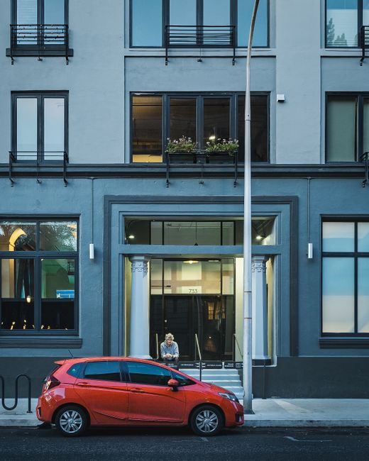 Modern red automobile parked on sidewalk near residential building with windows on street with streetlamp and asphalt road in city