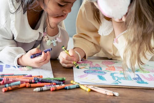Free Crop multiethnic little girls leaning on hands and drawing greeting poster while preparing for Easter celebration together Stock Photo