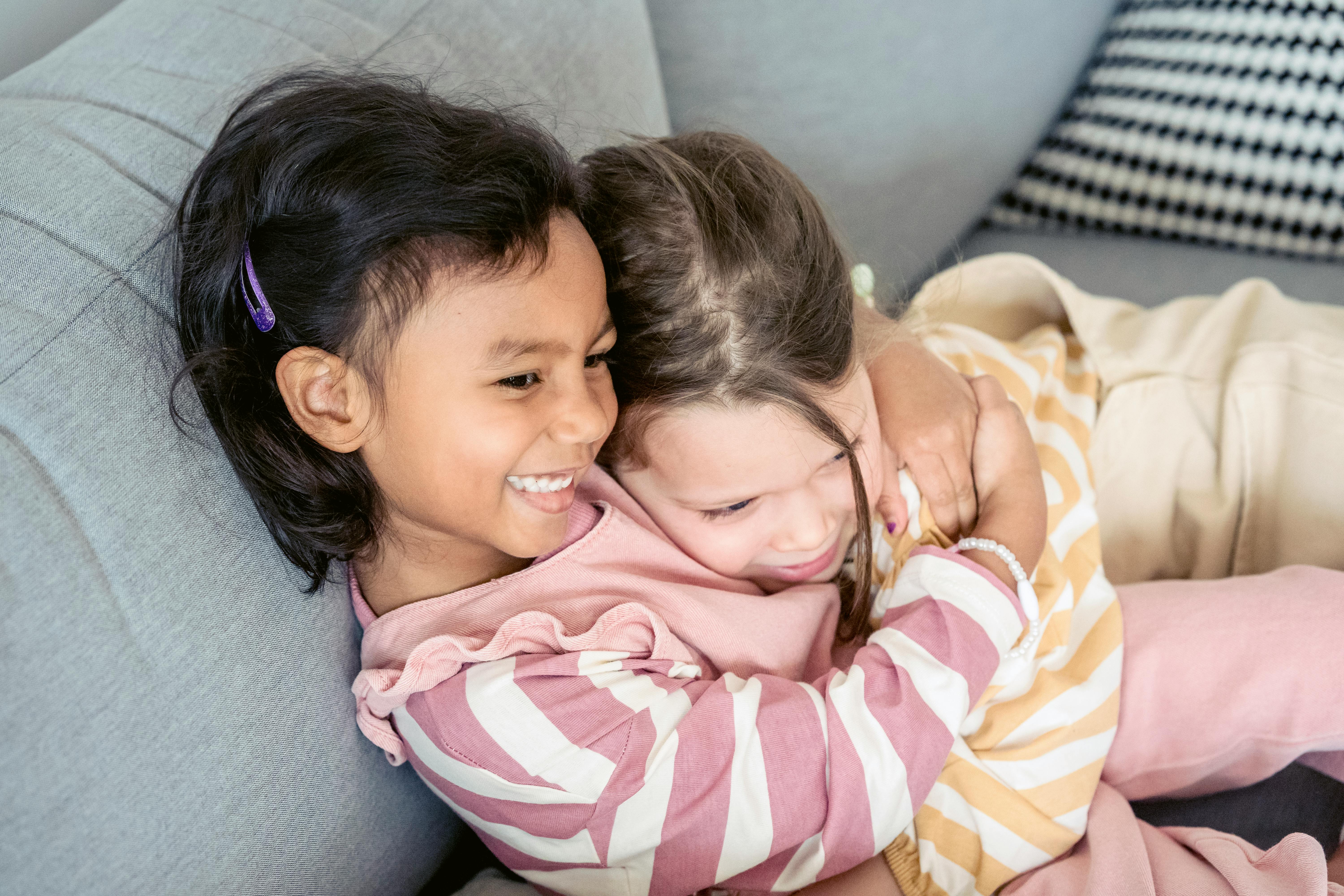 cute diverse girls hugging tenderly on couch