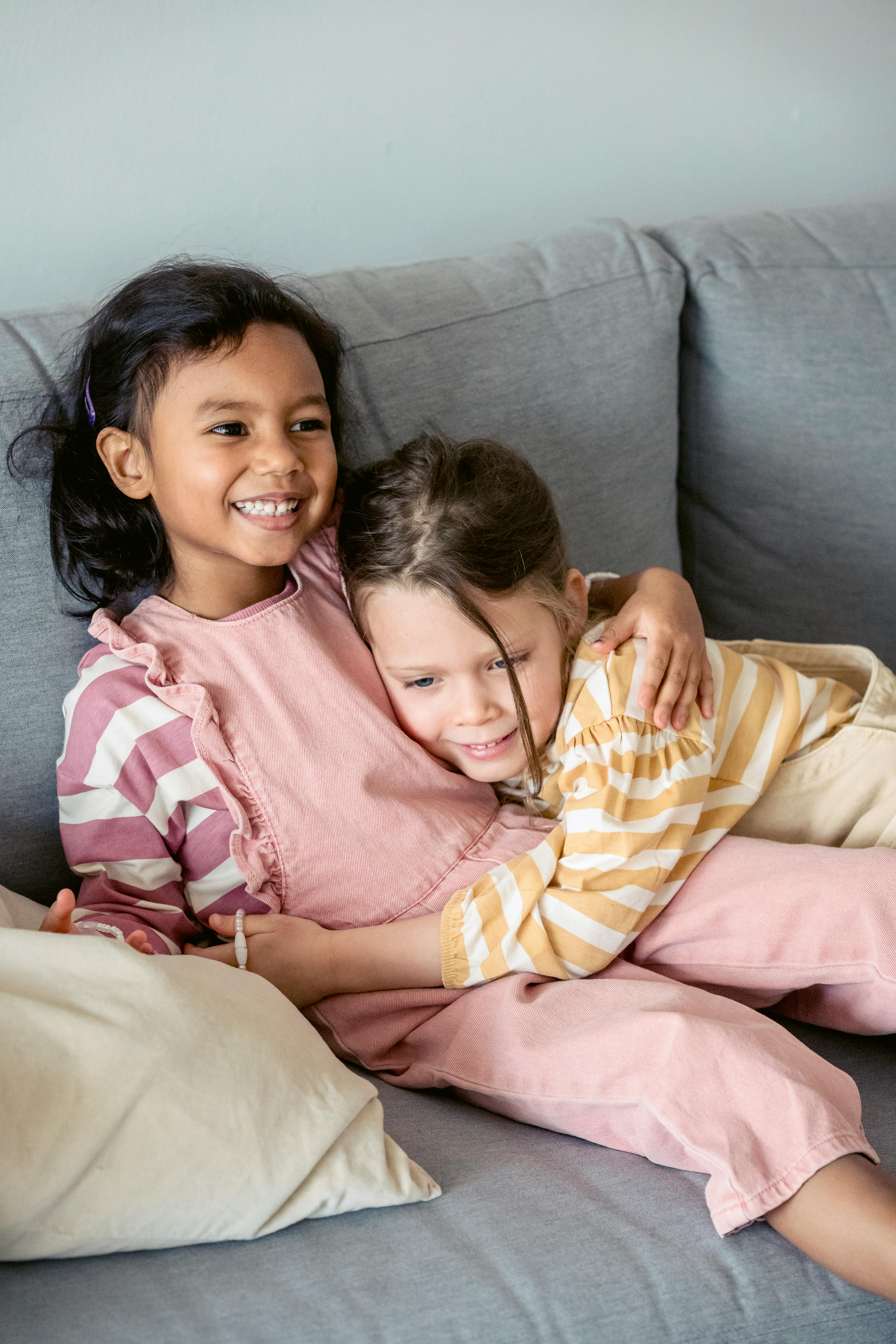 smiling multiethnic girls hugging on sofa