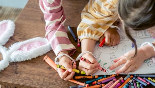Free High angle of crop anonymous sisters painting with colorful crayons on coloring picture for Easter holiday Stock Photo