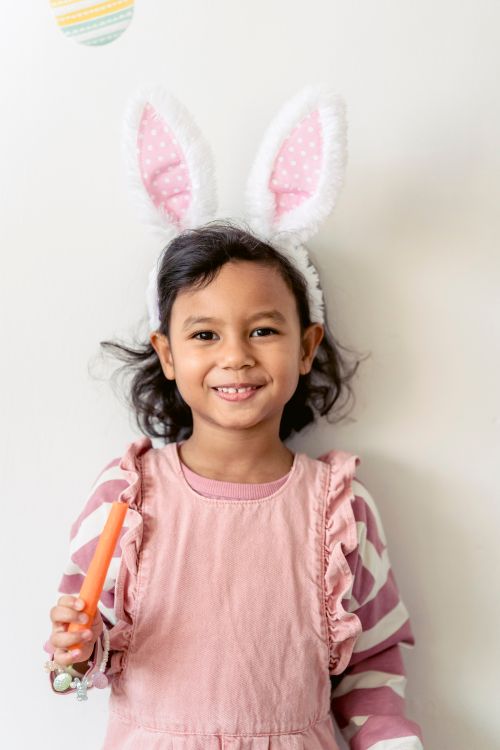 Free Adorable preschool girl wearing bunny ears for Easter celebration standing with carrot and smiling at camera Stock Photo