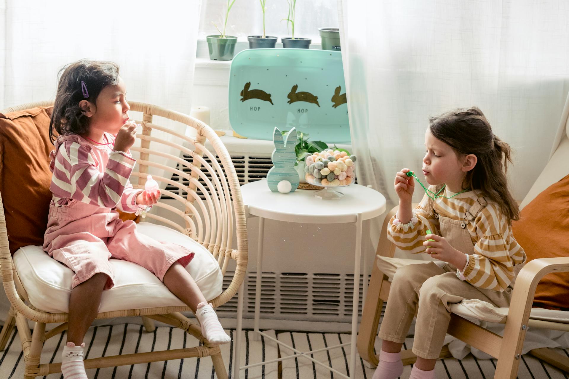 High angle of multiethnic little friends sitting in armchairs near table with decorative bunny in bedroom