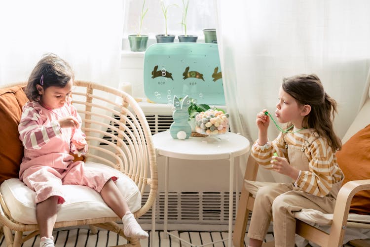 Multiethnic Girls Blowing Soap Bubbles While Sitting Near Window