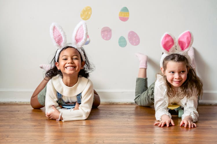 Smiling Girls In Bunny Ears Lying On Floor At Home