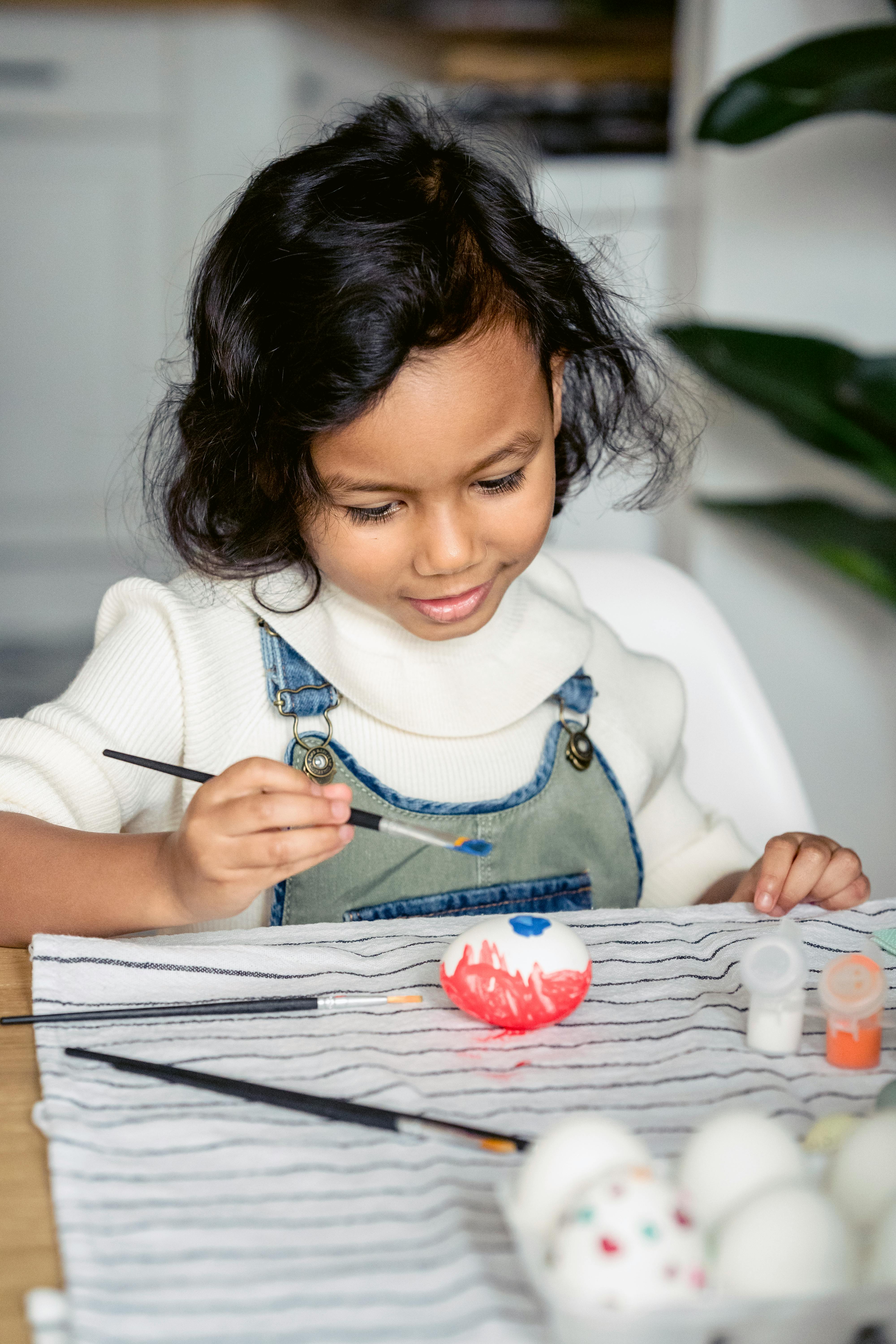 Young girl engaged in Easter egg painting activity at home.