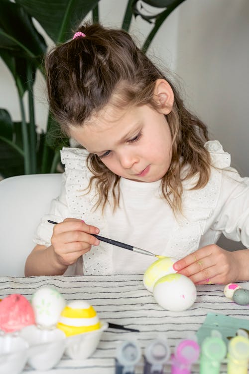 Adorable girl painting eggs with paintbrush
