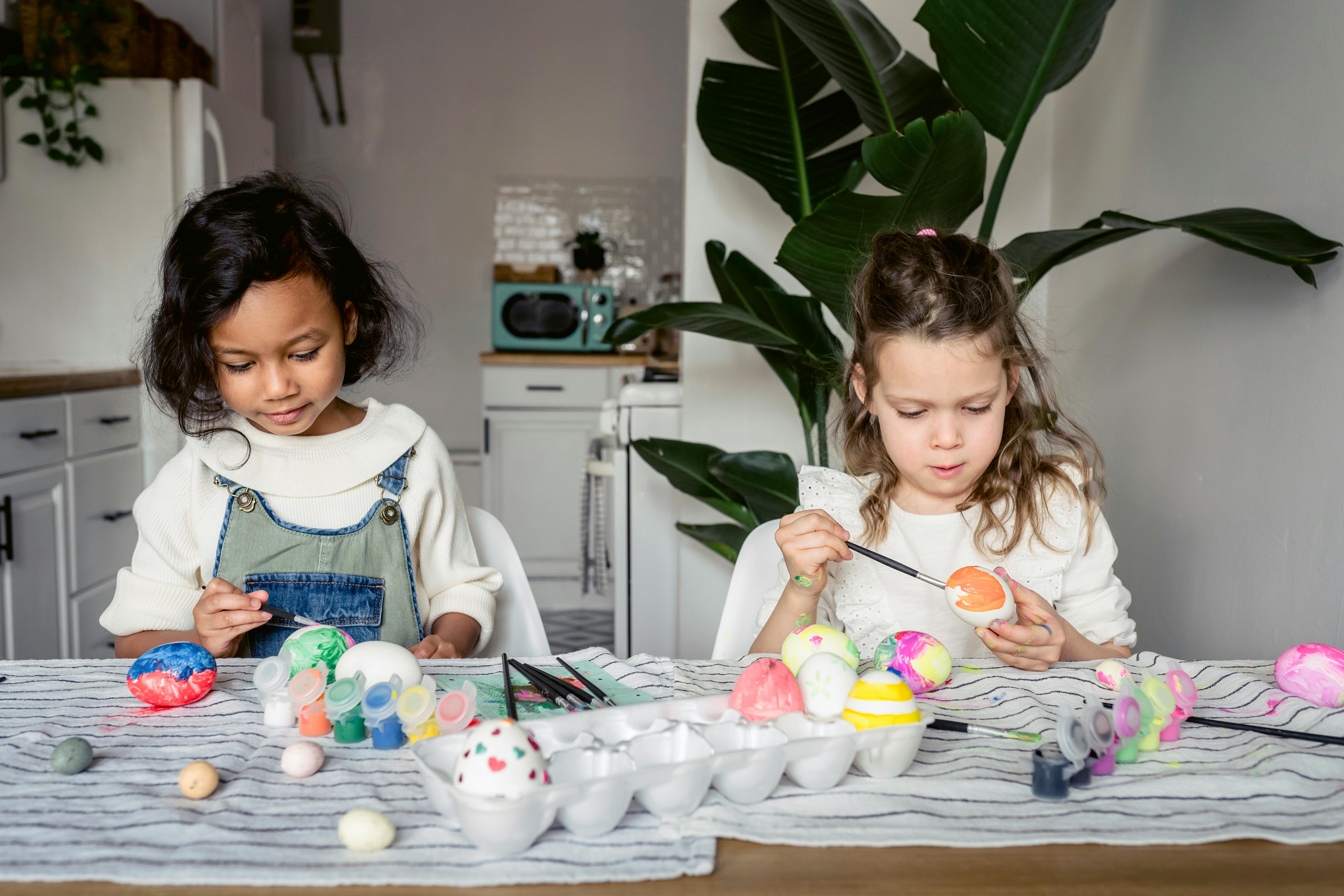 focused multiracial girls painting eggs in kitchen