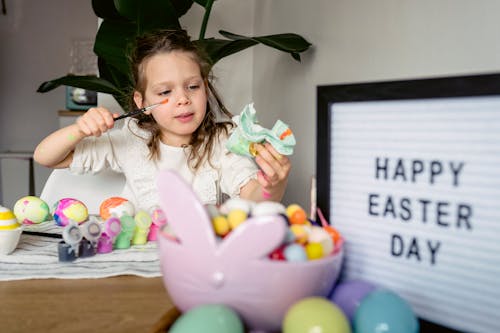 Cute girl painting eggs at table with signboard