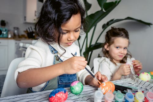 Attentive diverse girls painting eggs for Easter holiday