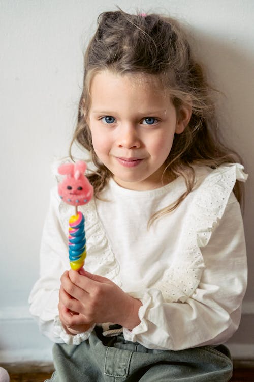 Little adorable girl with toy smiling and looking at camera while leaning on wall