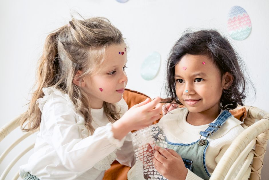 Cheerful diverse cute children smiling and decorating faces while having fun with small stickers in daytime