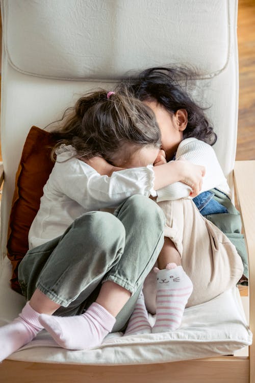 Loving little sisters embracing gently in armchair