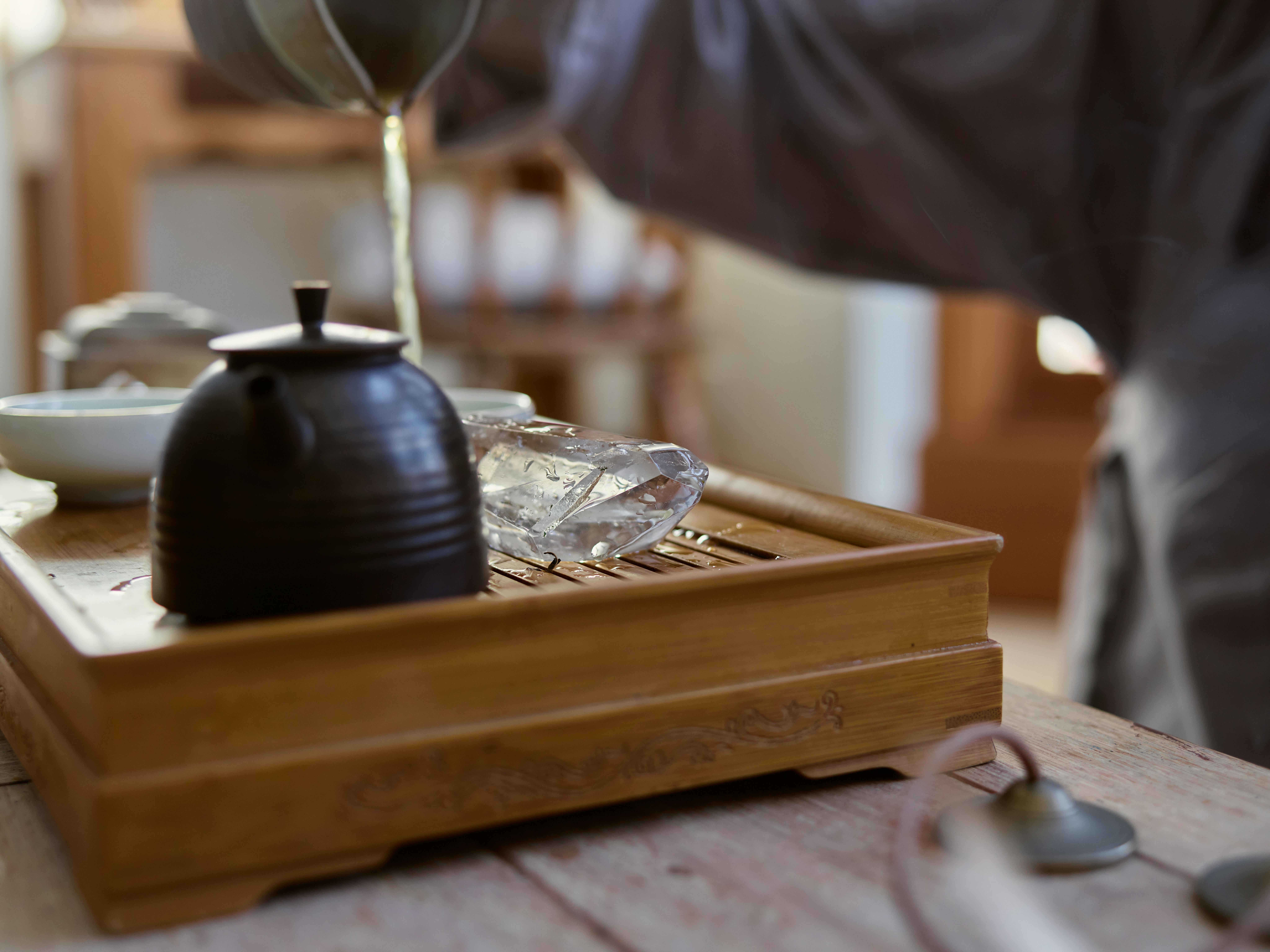 A serene scene of tea being poured into a rustic teapot on a wooden tray indoors.