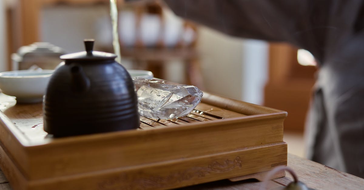 A serene scene of tea being poured into a rustic teapot on a wooden tray indoors.