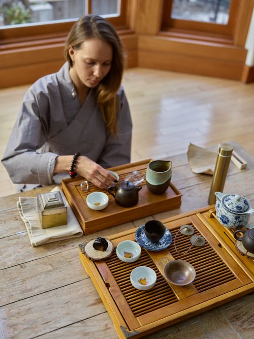 Free Woman performing a traditional tea ceremony indoors, featuring a beautiful tea set on a wooden table. Stock Photo