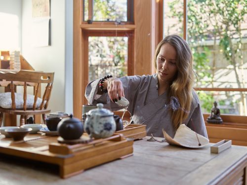 Free A woman performs a serene tea ceremony in a sunlit room with traditional teaware. Stock Photo