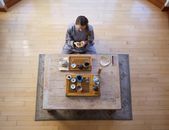 Man in Gray Long Sleeve Shirt and Black Pants Sitting on Brown Wooden Table