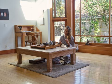 Woman enjoying a peaceful tea ceremony in a serene, sunlit room with a wooden interior.