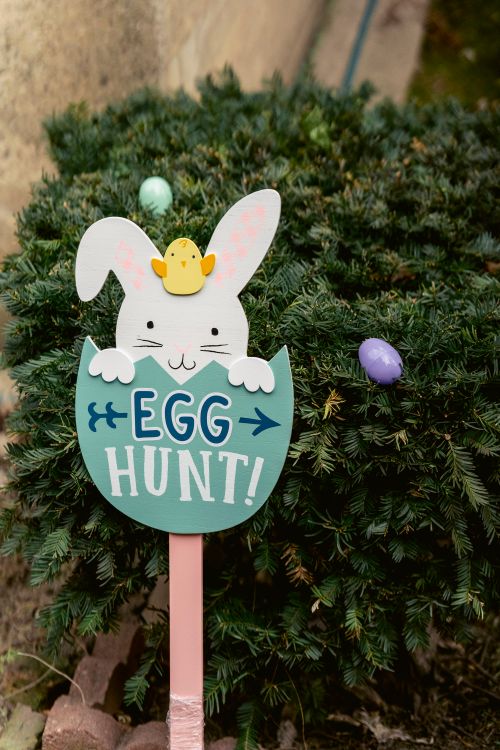 Free Decorative sign with inscription and bunny placed near green branches of tree with colorful eggs during Easter celebration on street Stock Photo