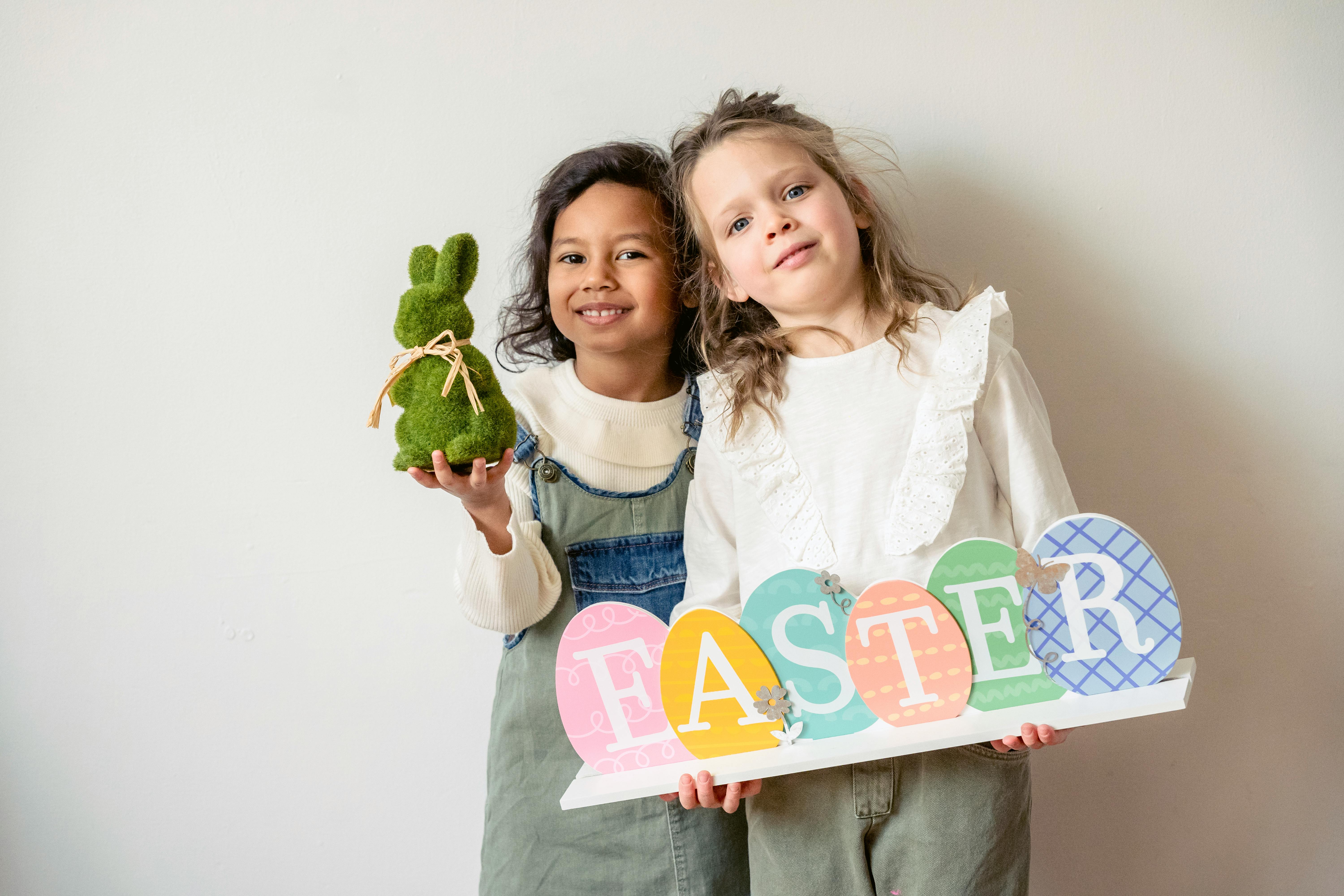 cheerful diverse girls showing easter decorations near wall