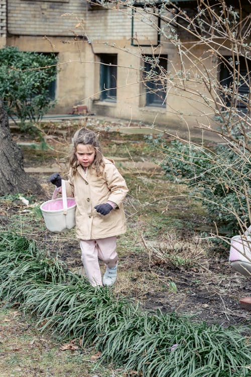 Free Full body girl in warm clothes looking for egg during Easter hunt in spring garden Stock Photo