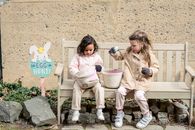 Full body positive cute diverse girls in warm clothes playing with Easter eggs and sitting on bench in backyard
