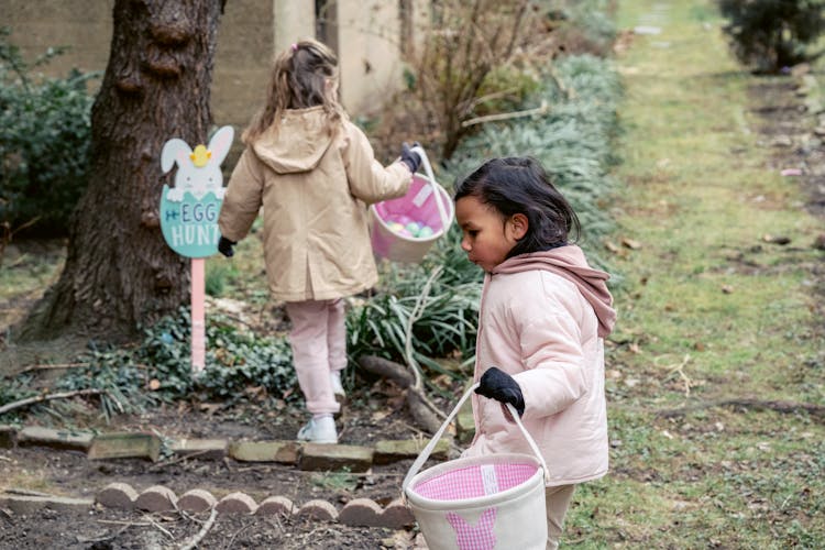 Girls With Baskets Collecting Easter Eggs In Garden