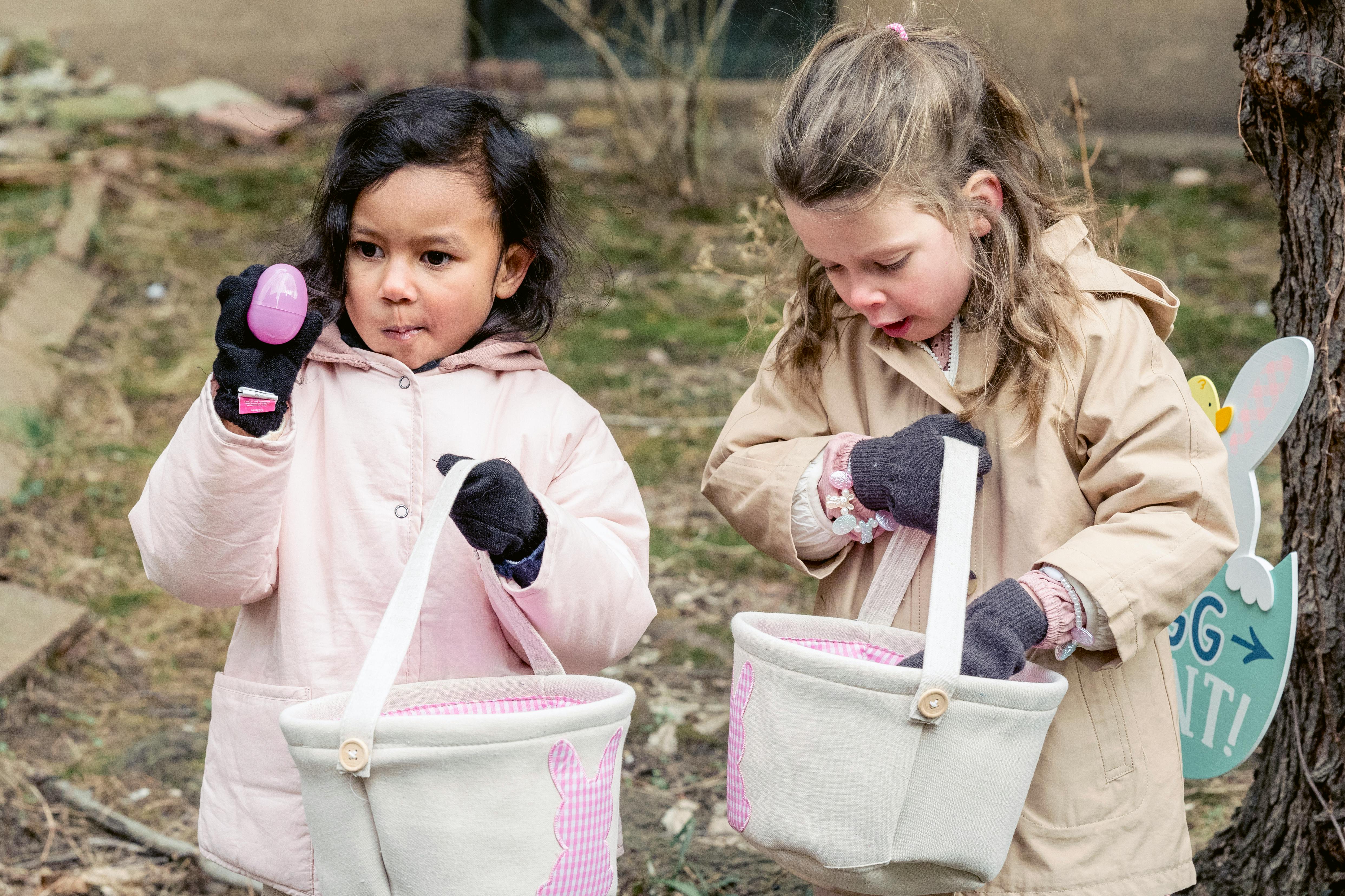 curious diverse girls collecting easter eggs into baskets in park