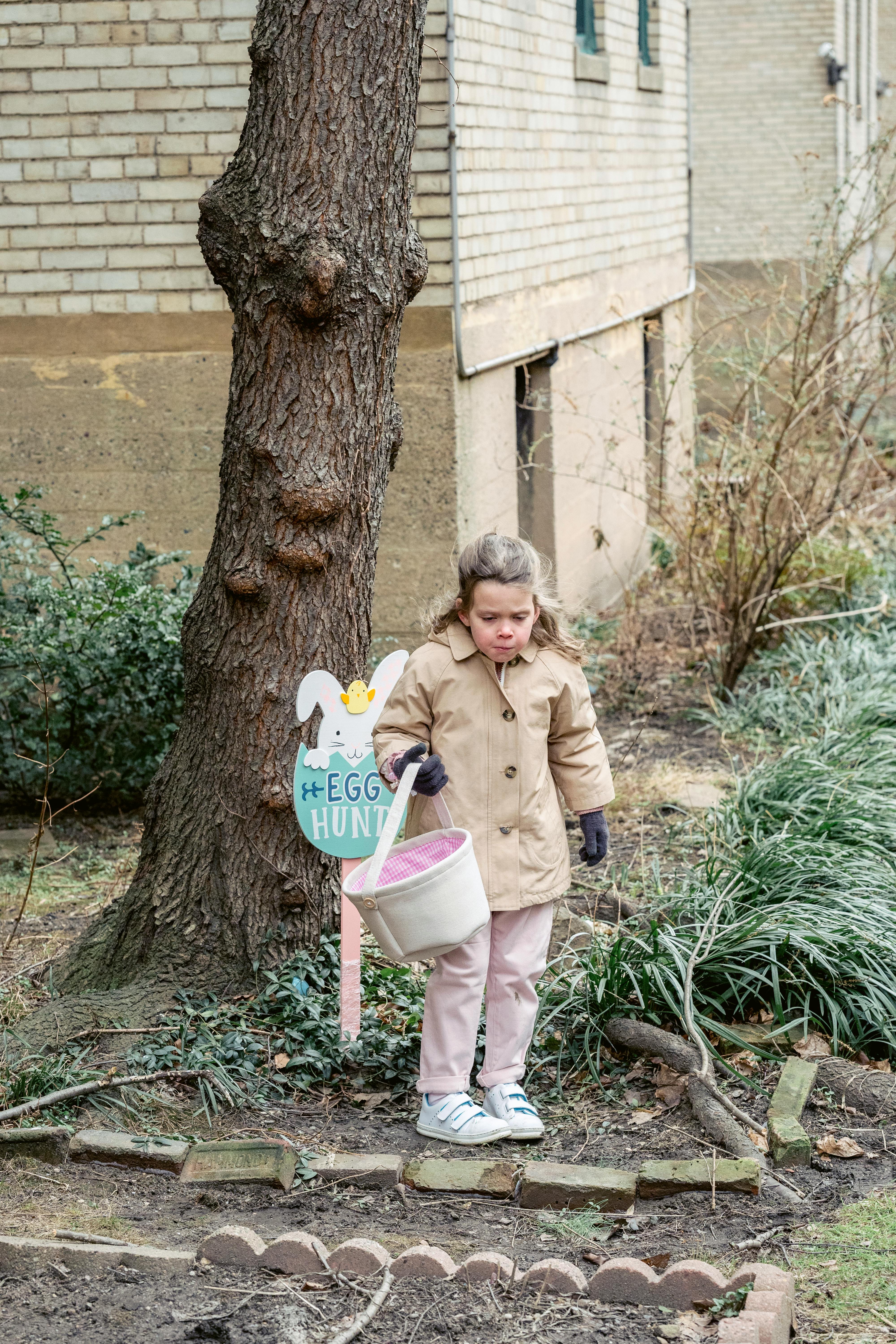 little girl with basket collecting easter eggs in park