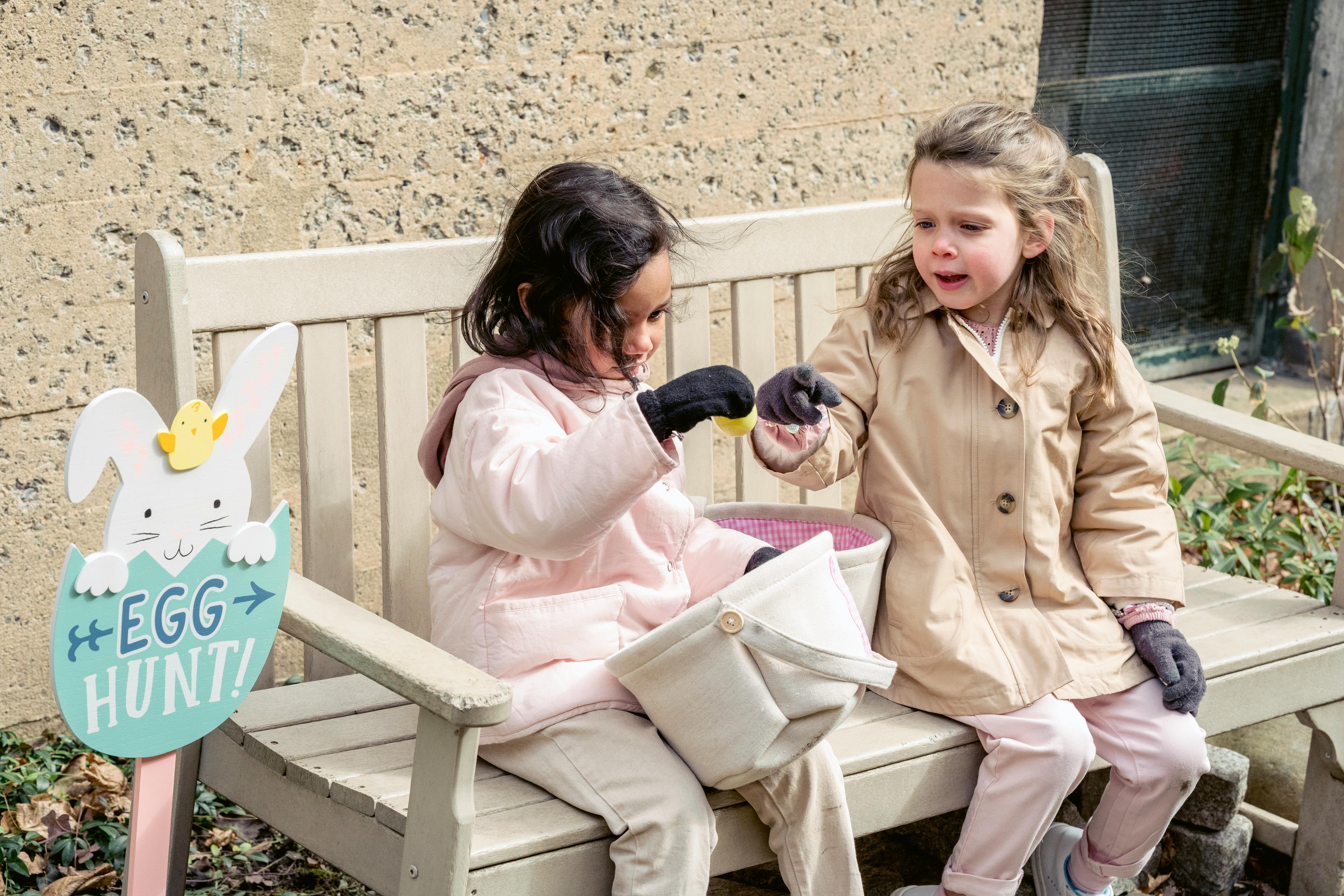 cute diverse girls playing with easter eggs on garden bench